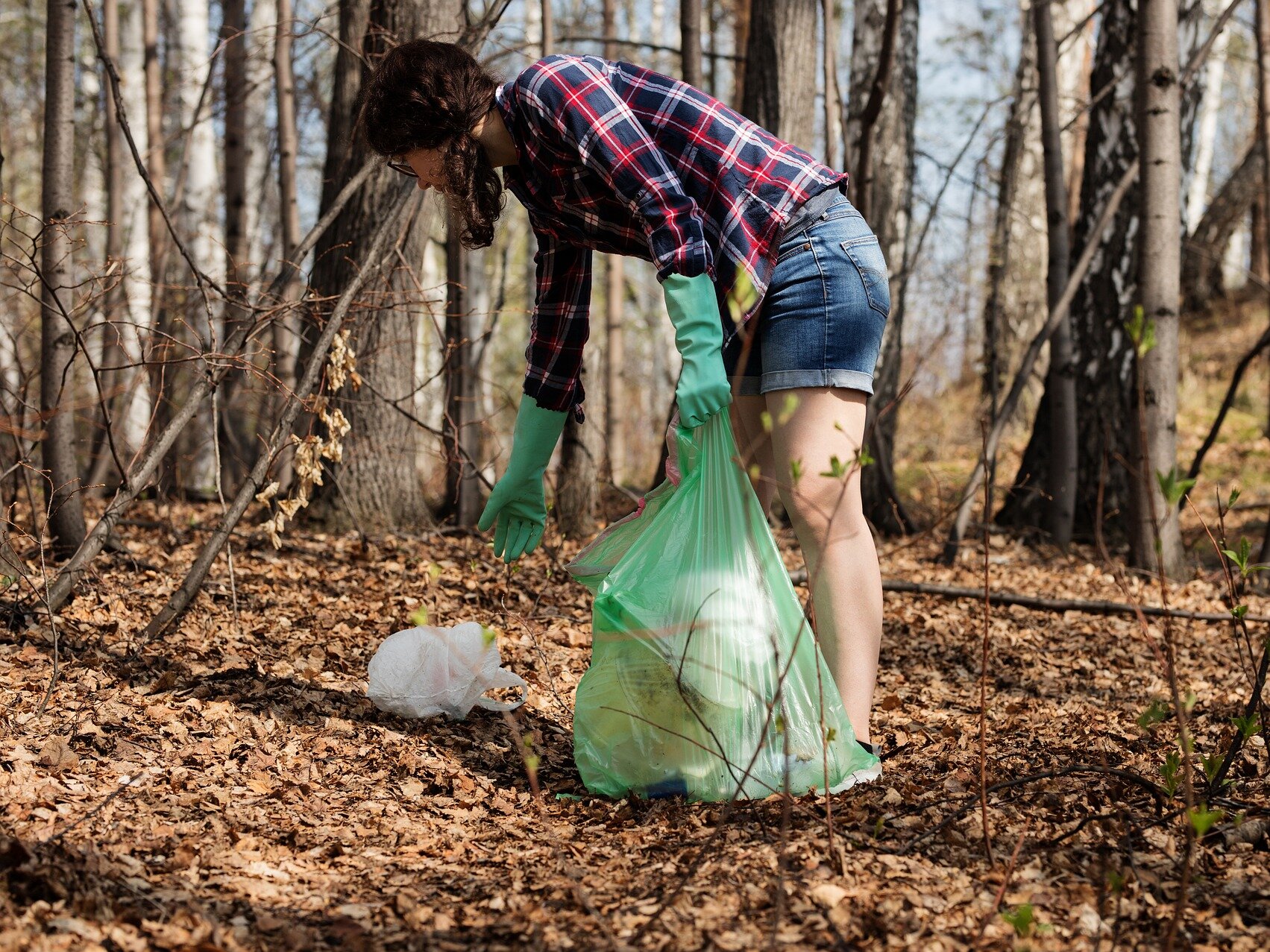 Frau sammelt im Wald Müll ein.