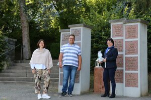 Drei Personen vor der Urnenwand auf dem Friedhof.