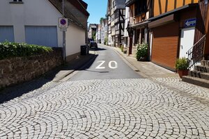 Bild der Chaldäergasse Herborn. Im Vordergrund ist die gepflasterte Einfahrt der Gasse zu sehen, im Hintergrund die Oberfläche aus Asphalt, die durch Pflastersteine ersetzt wird. 